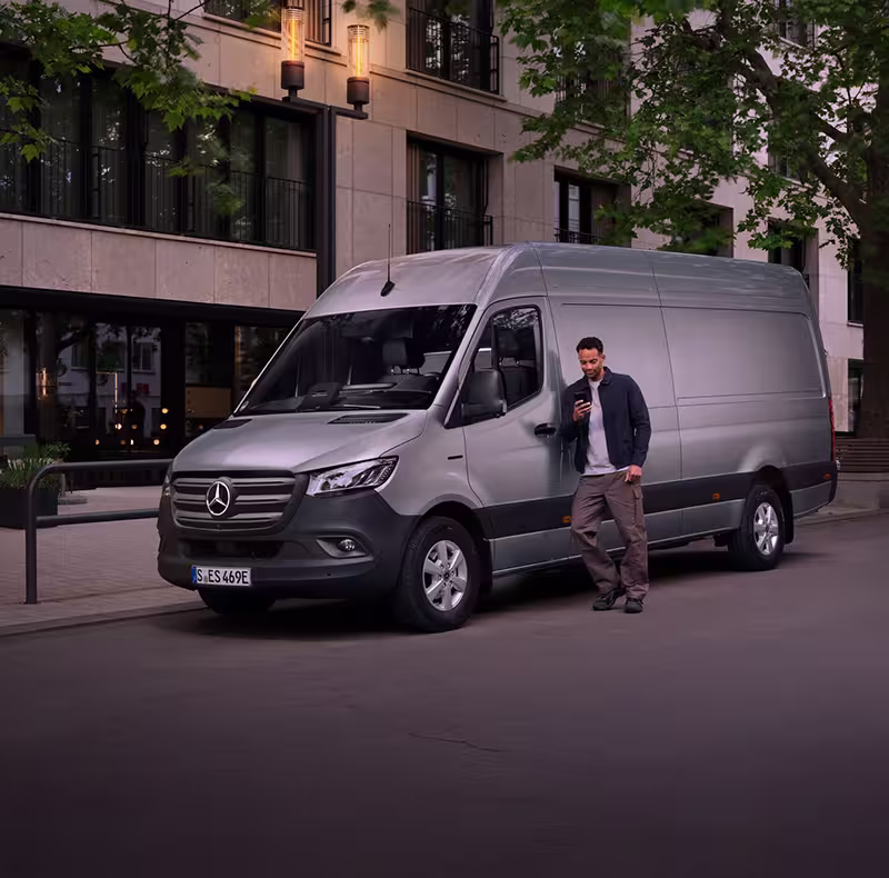 Van Elektrisch in der Stadt, Mann steht mit Handy vor dem Fahrzeug